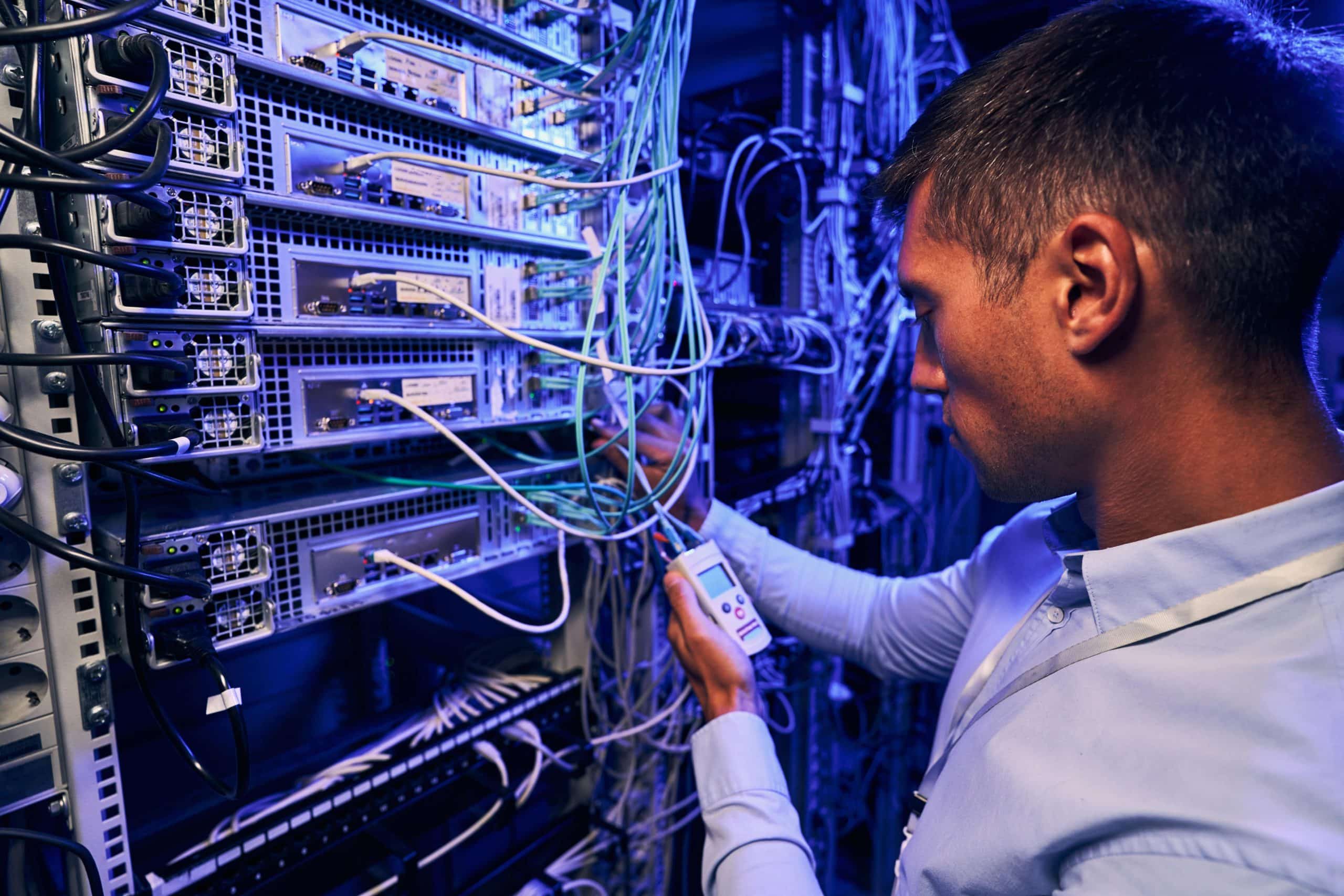 Técnico de redes trabajando en un centro de datos, verificando las conexiones de cableado estructurado en un rack de servidores.
